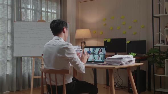 Back View Of Asian Man Having Video Call On Laptop While Working With Documents At The Office