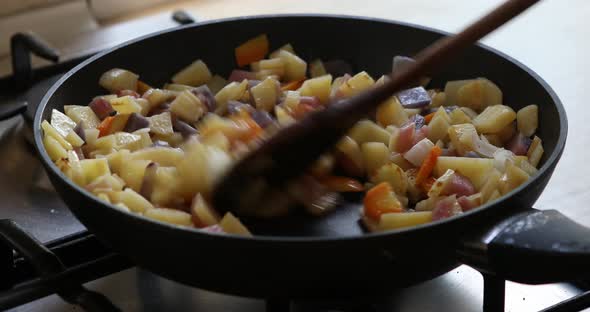 Woman stirring cut raw potatoes in frying pan, closeup. Vegan food