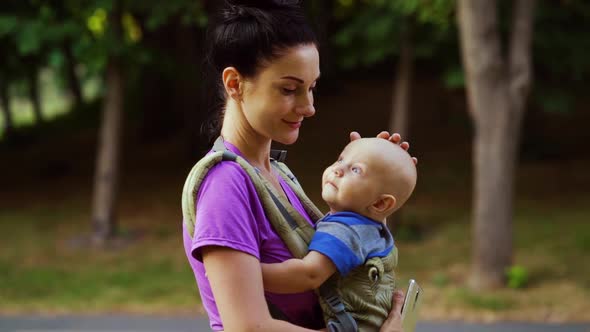 Loving Mother Carrying Baby in Sling During Walk in Park