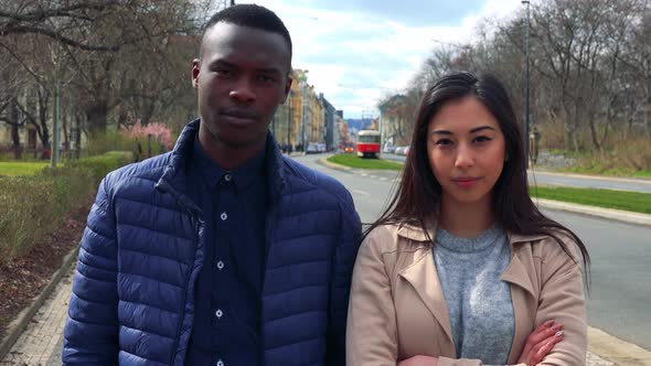 A Young Black Man and a Young Asian Woman Shake Their Heads at the Camera in a Street in Urban Area