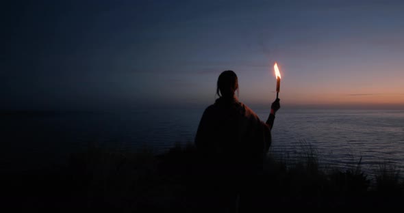 Young girl holds a fire torch at sunset 