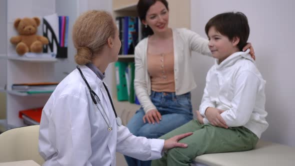 Side View Positive Doctor Talking to Little Patient and Looking at Camera Smiling As Happy Son and