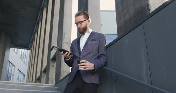 Office Manager in Business Clothes which Using His Mobile on the Steps of Business Center