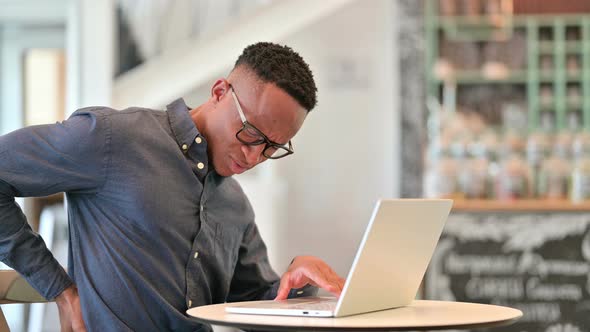 Tired African Man with Laptop Having Back Pain in Cafe 