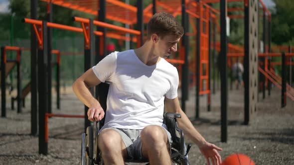 Young Smiling Man in Wheelchair Bouncing Ball in Slow Motion and Looking at Camera