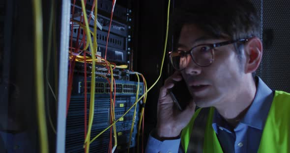 Asian male it technician using smartphone checking computer server