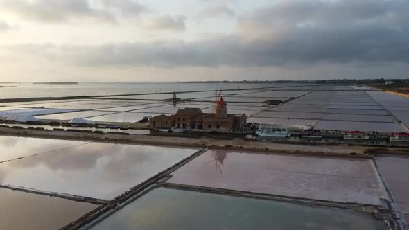 Drone Flying Towards The Windmill In The Salt Pans In Marsala, Sicily, Italy During Sunset - aerial