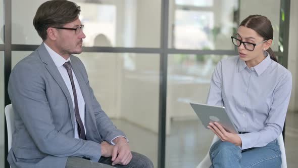 Young Female with Tablet Interviewing Middle Aged Businessman