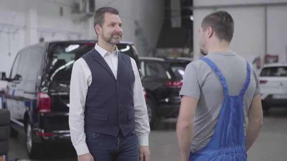 Portrait of Smiling Caucasian Man Taking His Car After Repair, Young Auto Mechanic Giving Car Keys