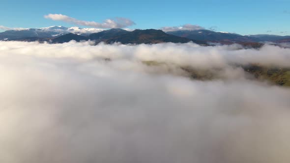 Aerial View of Vibrant Sunset Over White Dense Clouds with Distant Dark Mountains on Horizon