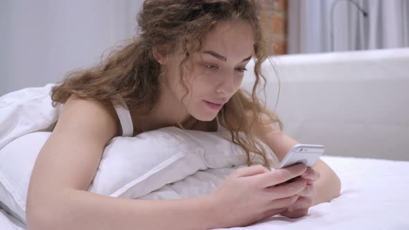 Female Lying in Bed Using Phone for Browsing Online