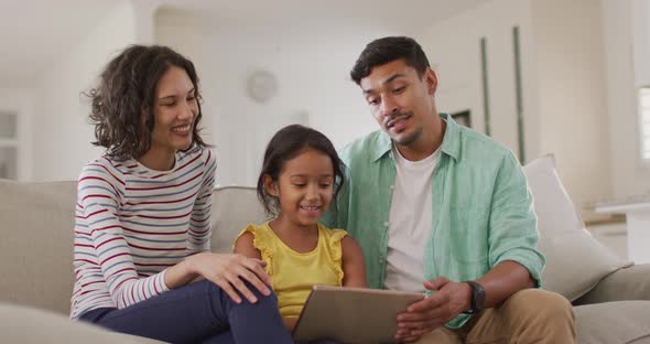 Happy hispanic parents and daughter sitting on sofa using laptop