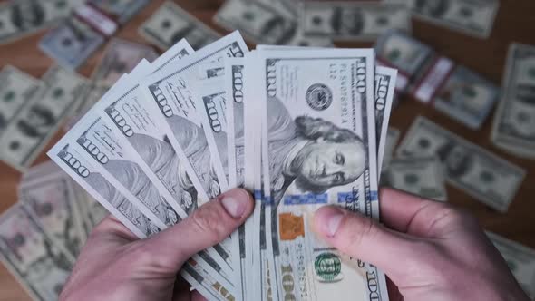 Dollars in Male Hands on Background of Table with Money