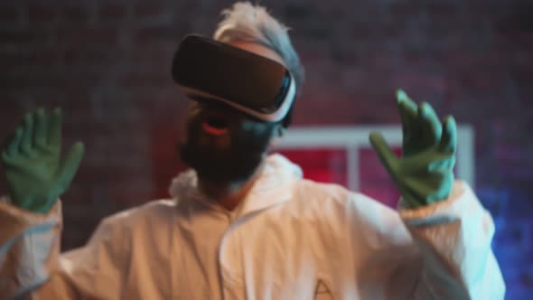 Excited Man Wearing Protective Suit and Virtual Reality Headset Dancing Indoors