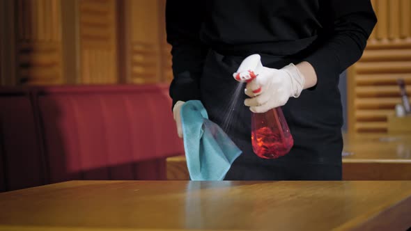 Closeup a Waiter in Protective Gloves Wipes Restaurant Tables Using an Antiseptic Spray and a