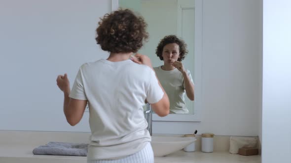 A Cheerful Woman Dances in the Bathroom in Front of a Mirror While Brushing Her Teeth