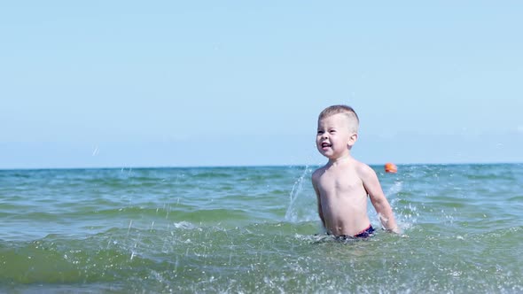 Happy Caucasian Baby Kid Boy Splashing Playing in Sea Ocean Water in Sunny Day