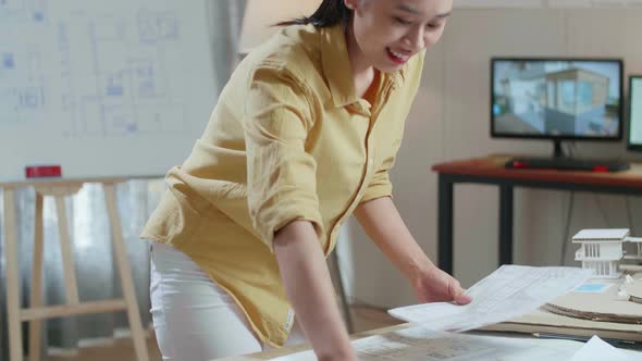 Asian Woman Engineer With A Laptop Looking At Blueprint While Working At The Office