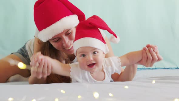 Smiling Santa Child Lying in Santa Claus Costume, in Red Hat with Mother.