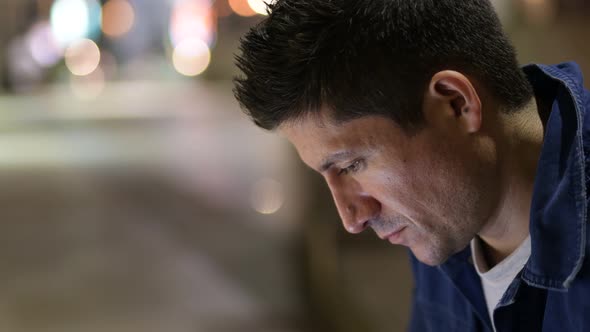 Hispanic Man Looking Down While Thinking in the City Streets at Night