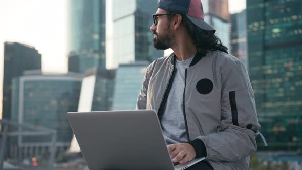 Handsome Young Man Sitting on the Street at the Business Center with a Laptop