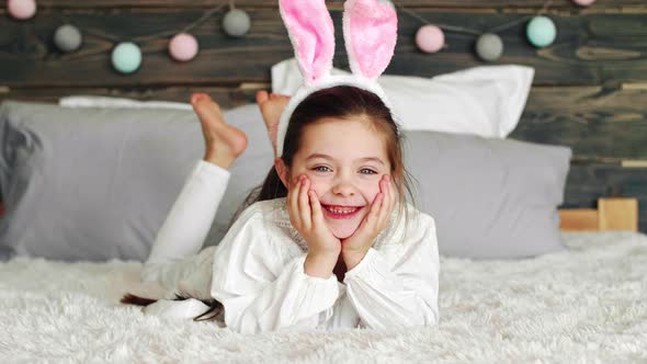 Smiling girl with bunny ears lying on the bed