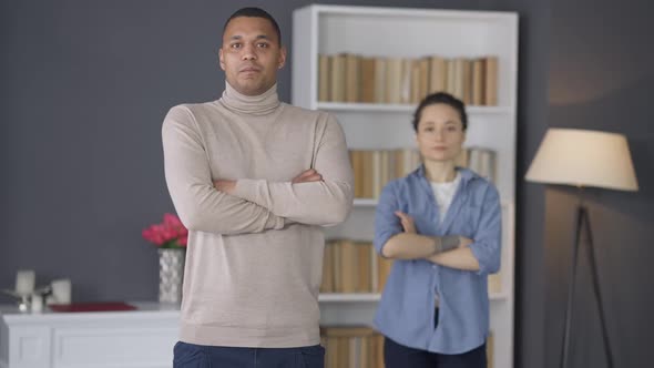 Young Confident African American Man Crossing Hands Looking at Camera with Blurred Caucasian Woman