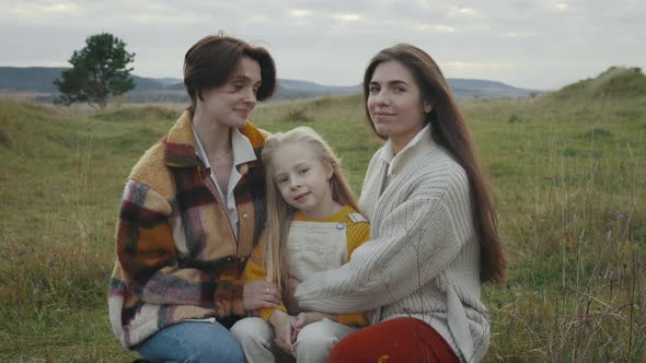 Two Lesbians Embracing Their Daughter on Nature