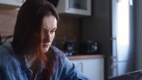 Woman Working at Laptop While Sitting at the Table in the Kitchen at Home