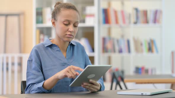 Attractive African Woman Celebrating Success on Tablet in Library