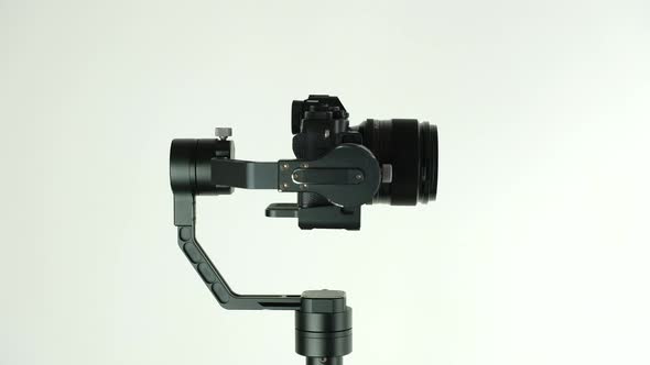 Gimbal with digital camera rotates on white background.