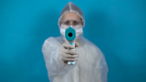 Young Woman in a Protective Suit with an Infrared Thermometer. The Girl Measures the Temperature