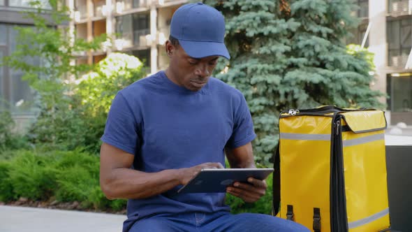 Camera Zoom in African Man Courier Food Delivery Uses Tablet Looking Camera