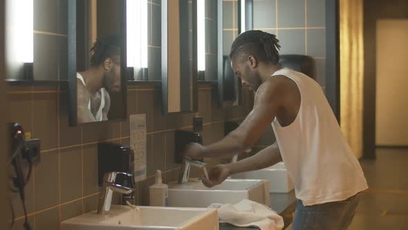 Side View of Young African American Man Approaching To Sink and Washing Face. Portrait of Relaxed