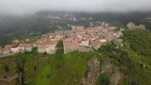 Aerial View Drone Flies Over Medieval Village on Hill Overlooking Misty Mountain Gorge