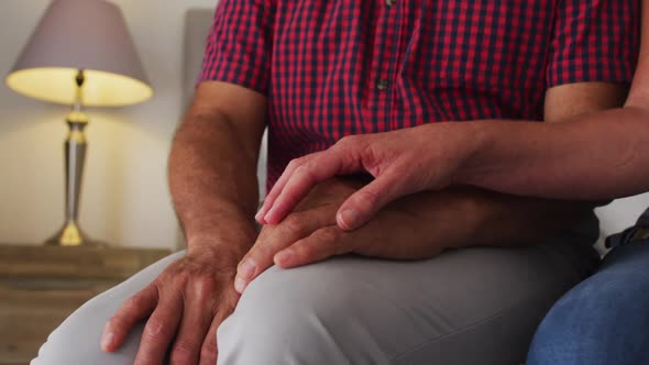 Mid section of caucasian senior couple holding hands at home