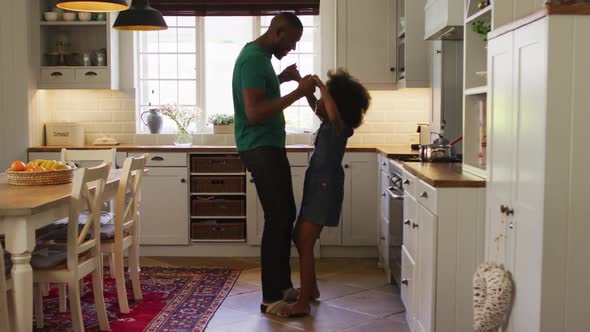 African american daughter and her father dancing together in kitchen