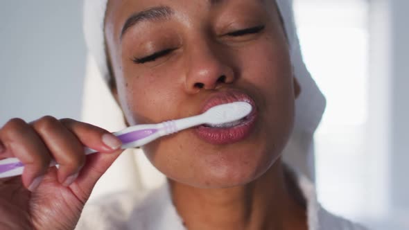 Portrait of african american woman in bathrobe brushing her teeth in the bathroom