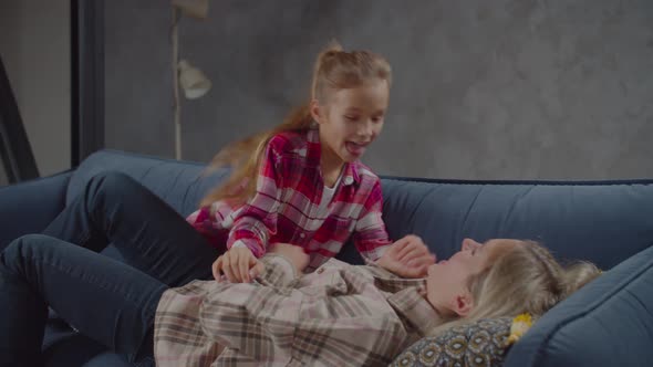 Laughing Daughter Tickling Joyful Mother on Sofa