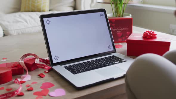 Hands of biracial woman holding waving while having valentine's video call on laptop