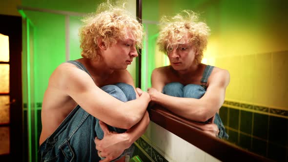 Depressed Sad Queer Man Crying Sitting in Bathroom Thinking Reflecting in Mirror