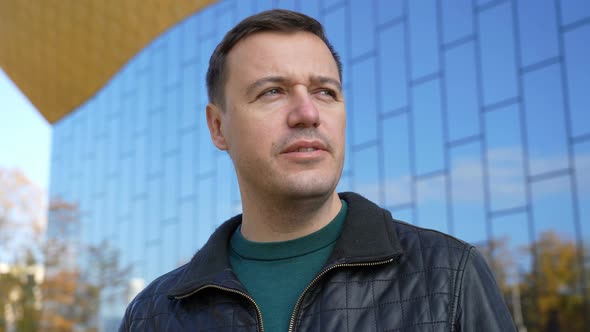 Businessman Standing Outdoors with Office Building in Background Looking at Camera and Talking