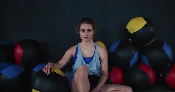Portrait of Young Attractive Athlete Woman Sitting on Gym Floor Near Cross Fit Balls Looking at