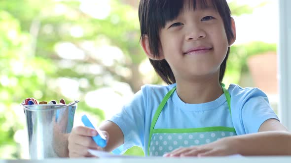 Cute Asian Child Drawing With Crayons On White Table