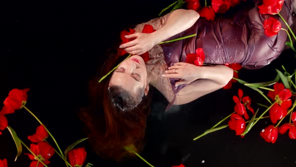 a Slender Girl in a Bath with Water Lies with Red Tulips