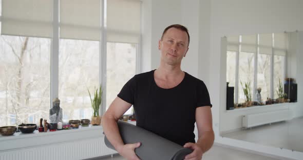 Portrait of a Male Yoga Trainer Holding Exercise Mat Standing in a Studio