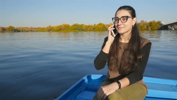 The Girl is Talking on the Phone While Sitting in a Boat on the Water