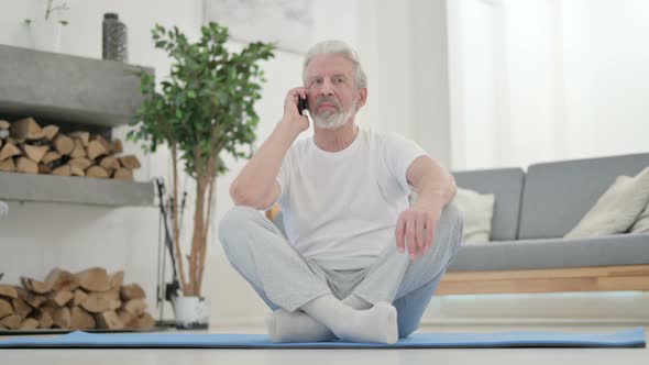 Old Man Talking on Smartphone on Yoga Mat at Home