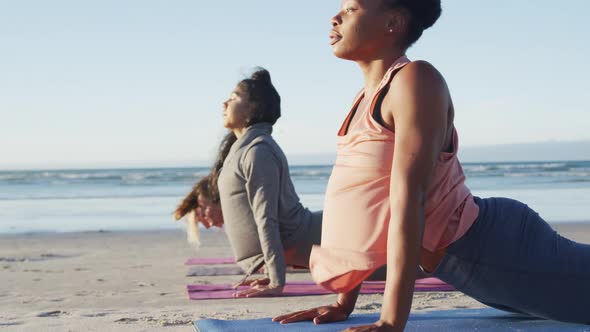 Group of diverse female friends practicing yoga, stretching at the beach