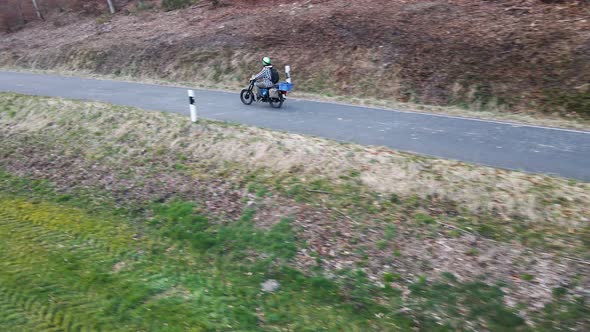 Drone view following a moped rider along an empty, narrow forest road in Germany. Wide angle trackin